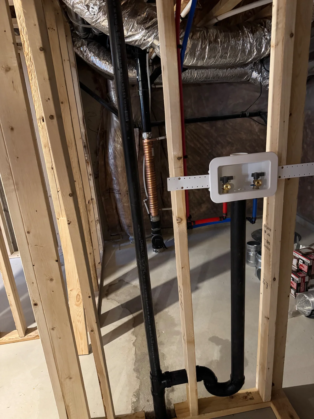 Laundry supply box with hot and cold valves beside ABS drain piping in an unfinished wall