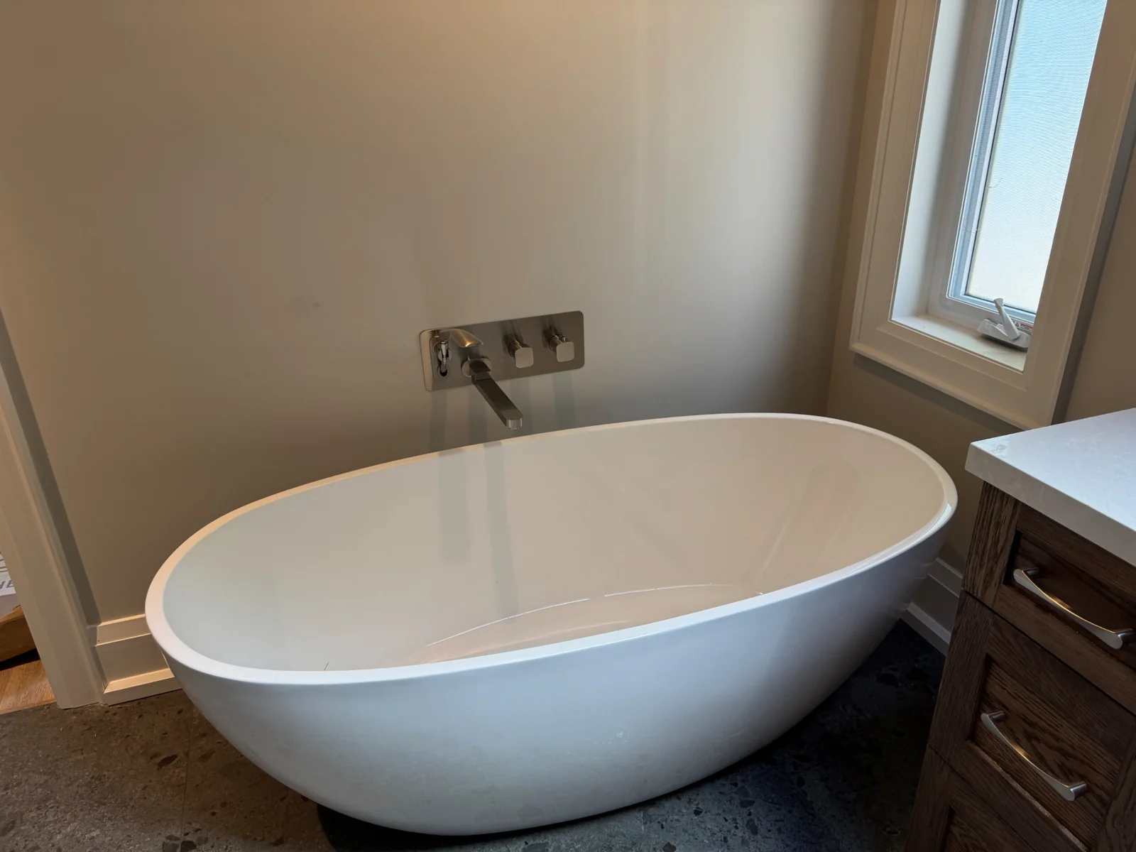 Freestanding white bathtub with wall-mounted tub filler beside a wood vanity