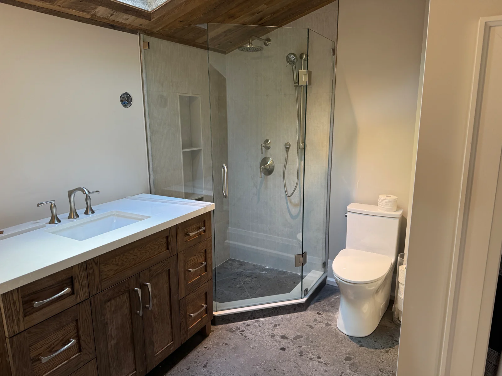 Plumb Bros finished bathroom with glass shower, wood vanity, chrome fixtures and toilet